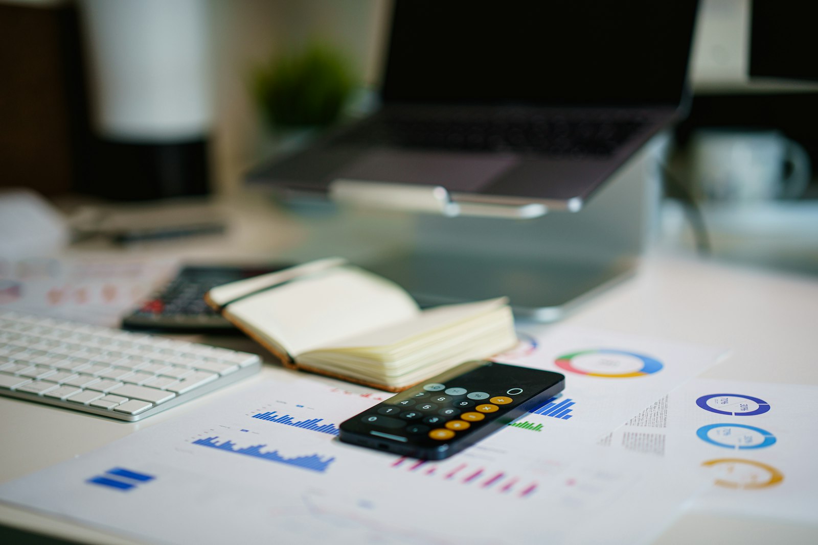 A desk with financial charts, a calculator, and a laptop