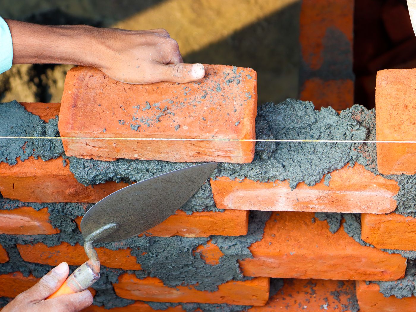 A mason bedding brick in mortar with a trowel