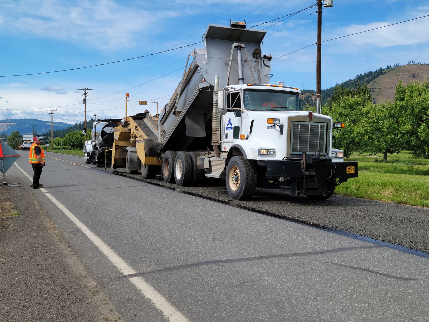 An asphalt paver and dump truck laying a road